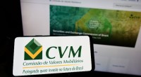 Celular com o logo da CVM e notebook aberto no site da Comissãod e Valores Mobiliários