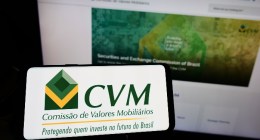 Celular com o logo da CVM e notebook aberto no site da Comissãod e Valores Mobiliários
