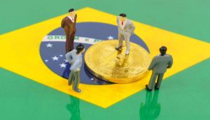 miniaturas de quatro pessoas diante de uma moeda de bitcoin em cima da bandeira do Brasil