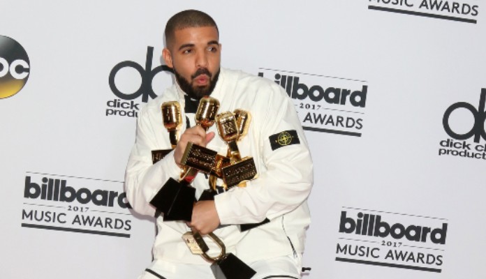 Drake, cantor e rapper, de terno branco segurando prêmios