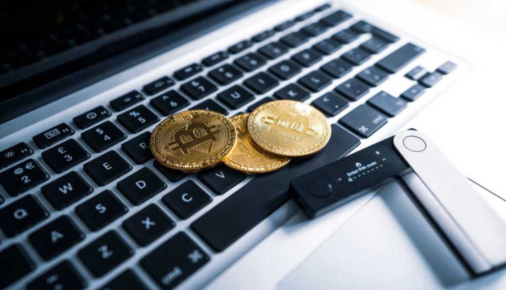 Moedas de bitcoin em cima de um teclado-ao lado uma cold wallet