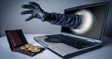Mão com luva preta sai de tela de computador emira uma carteira aberta com moedas douradas expostas