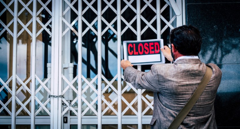 HOmem fixa placa de fechado -closed- em fachada de empresa