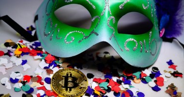 Moeda de bitcoin BTC entre confetes e máscara de carnaval