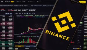 Smartphone mostra logotipo da Binance à frente de tela de negociação