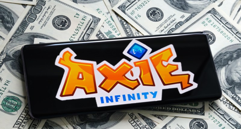 Smartphone por cima de notas de dólares mostra logo da Axie Infinity
