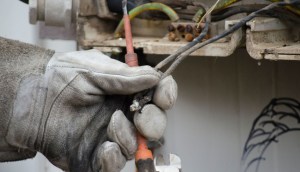 Mao com luva grossa tocando em fio de caixa de eletricidade