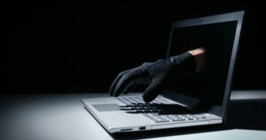 Mão de criminoso com luva preta saindo da tela de notebook em golpe financeiro na internet