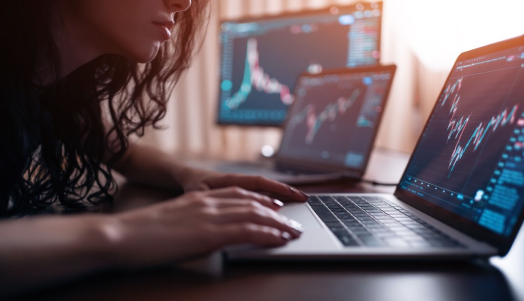 Mulher de cabelos compridos e ondulados operando gráficos de mercado em laptop