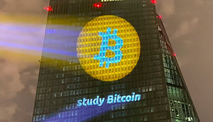 Logotipo do Bitcoin projetado no prédio do Banco Central Europeu com a frase "Study Bitcoin"