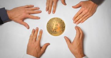 Várias mãos buscando pela moeda de bitcoin no centro de uma mesa