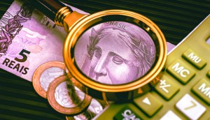 Lupa mostra rosto de nota de 5 reais- ao lado uma calculadora