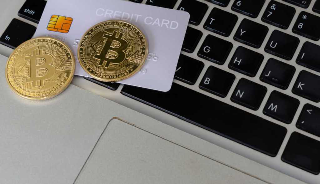 Moeda de bitcoin sob cartão de crédito sobrepostos em um teclado de laptop