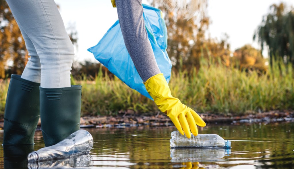 Pessoa se abaixa para pegar garrafa de plástico em rio