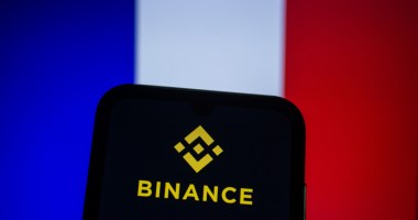 celular com logotipo da Binance e uma bandeira da França ao fundo