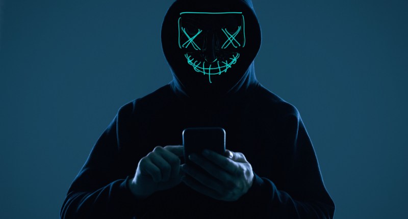 Hacker com capuz sorri no escuro