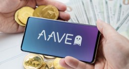 Uma mão segunra smartphone comlogomarca Aave e outra mãos critpomeodas Ethereum