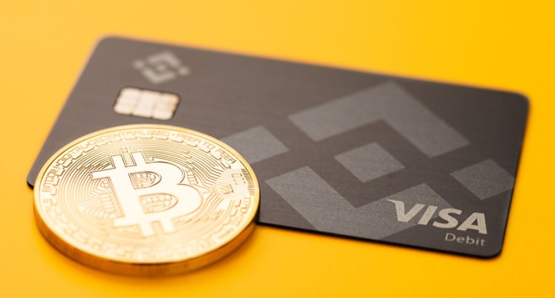 Cartão da Binance ao lado de moeda de Bitcoin