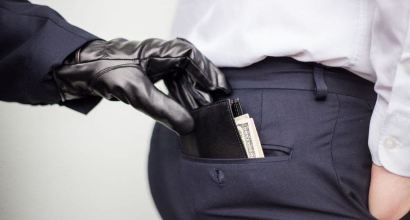Mão com luva preta subtraindo carteira de bolso traseiro de calça masculina