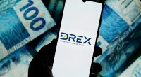 Tela de celular mostra logotipo Drex- no fundo notas de cem reais