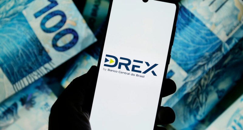 Tela de celular mostra logotipo Drex- no fundo notas de cem reais