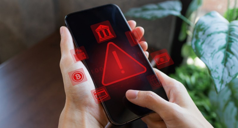 Uma pessoa segura um celular que mostra figuras grandes e vermelhas em formato triangular de alerta de vírus