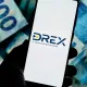 logo do drex em celular e notas de real ao fundo