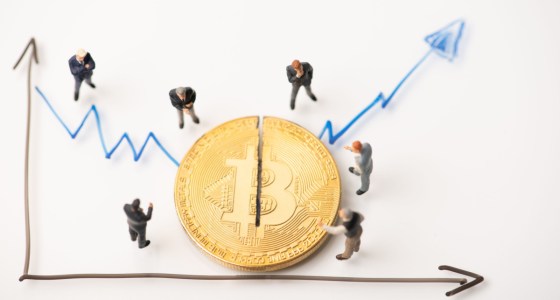 Ilustração de moeda gigante de Bitcoin observada por investidores e prestes a ser cortada ao meio