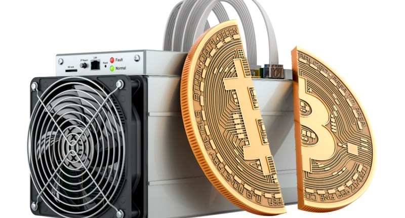moeda de bitcoin partida ao meio e apoiada em máquina de mineração