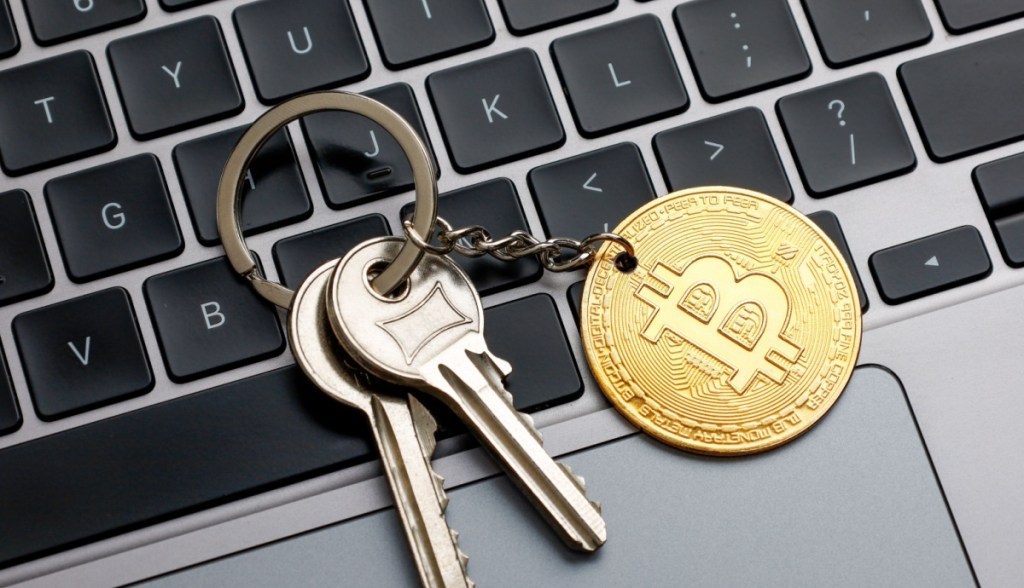 chaveiro com moeda de bitcoin em cima de teclado de laptop