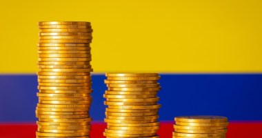 pilhas de moedas douradas à frente da bandeira da Colômbia