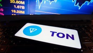 smartphone com logotipo da Toncoin TON à frente de monitor que mostra gráfico de mercado