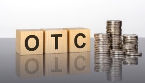 sigla OTC em cubos de madeira ao lado de pilhas de moedas
