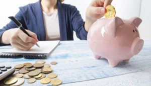 mulher insere moeda de Bitcoin em porquinho enquanto faz contas em um caderno